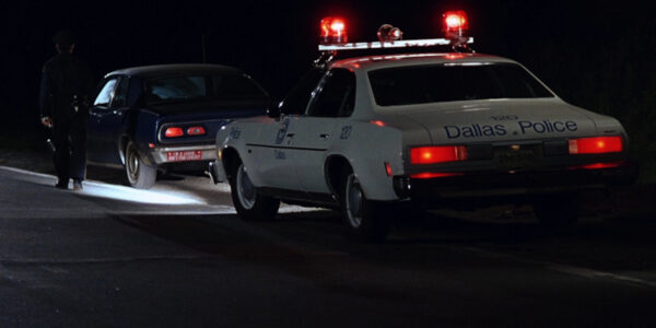 A police car with siren lights on pulls over a car at night