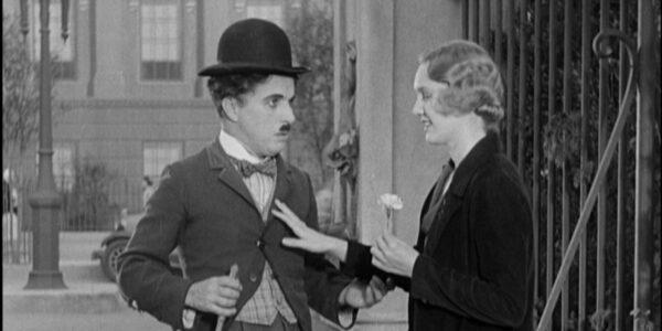 A little tramp in his bowler hat looks at a young woman holding a flower and smiling