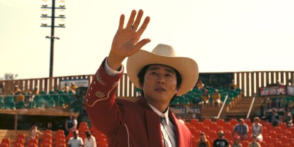 A man in a cowboy hat raises his hand at looks at the sky