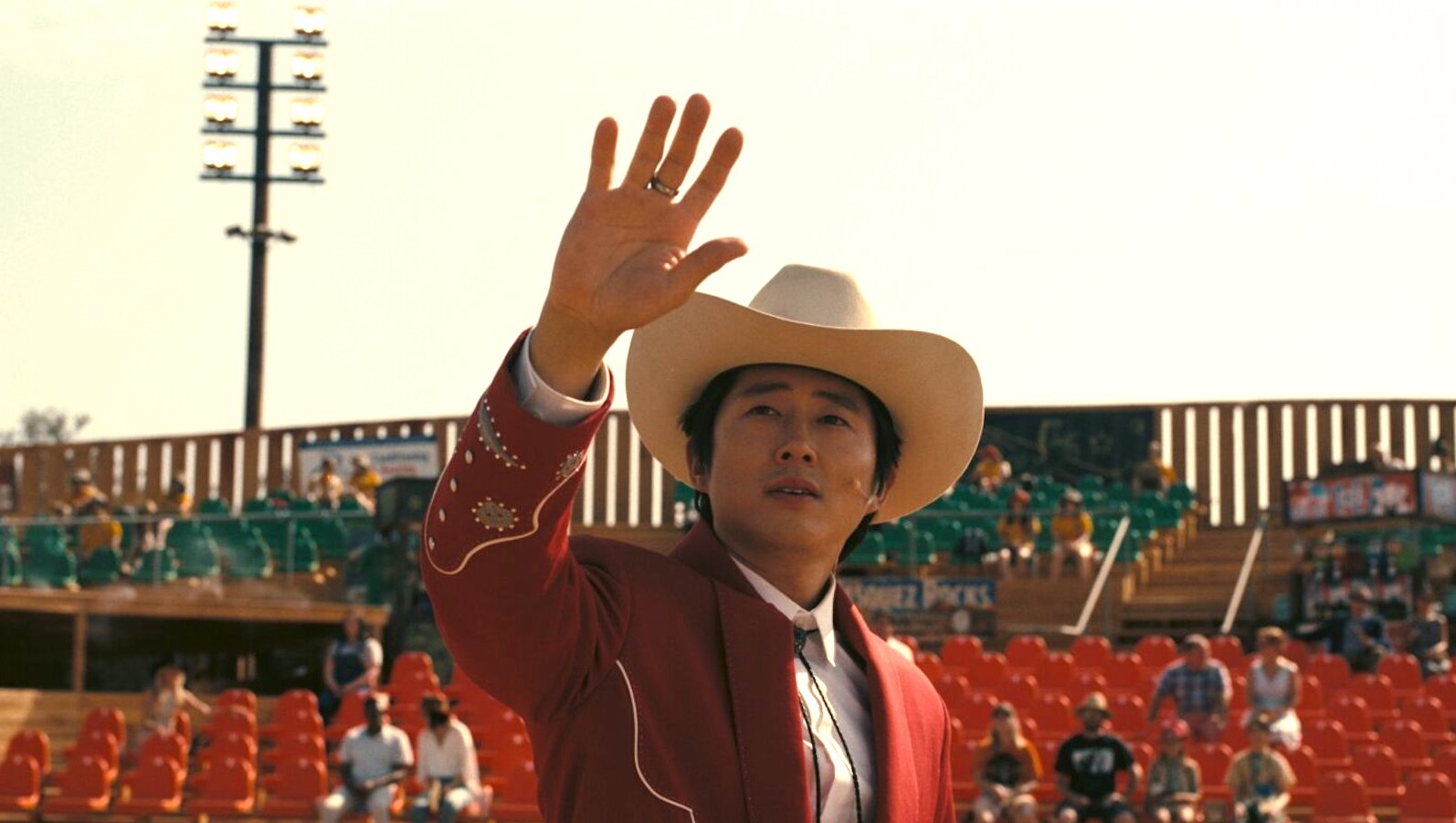 A man in a cowboy hat raises his hand at looks at the sky