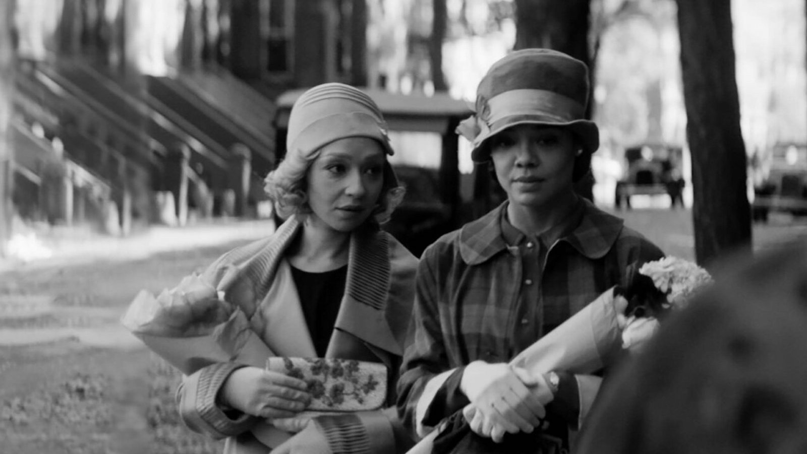 A black and white image of two women talking while walking down a New York street in the 1920s, wearing hats and gloves