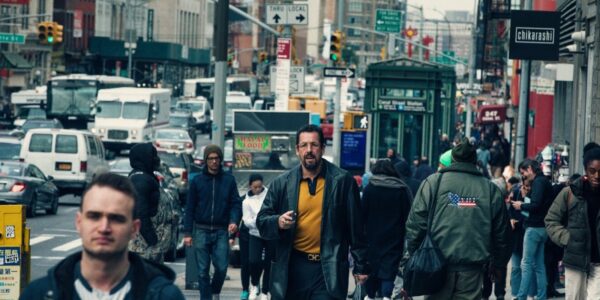 A man in yellow shirt and blue jacket walks through a crowded midtown NYC street