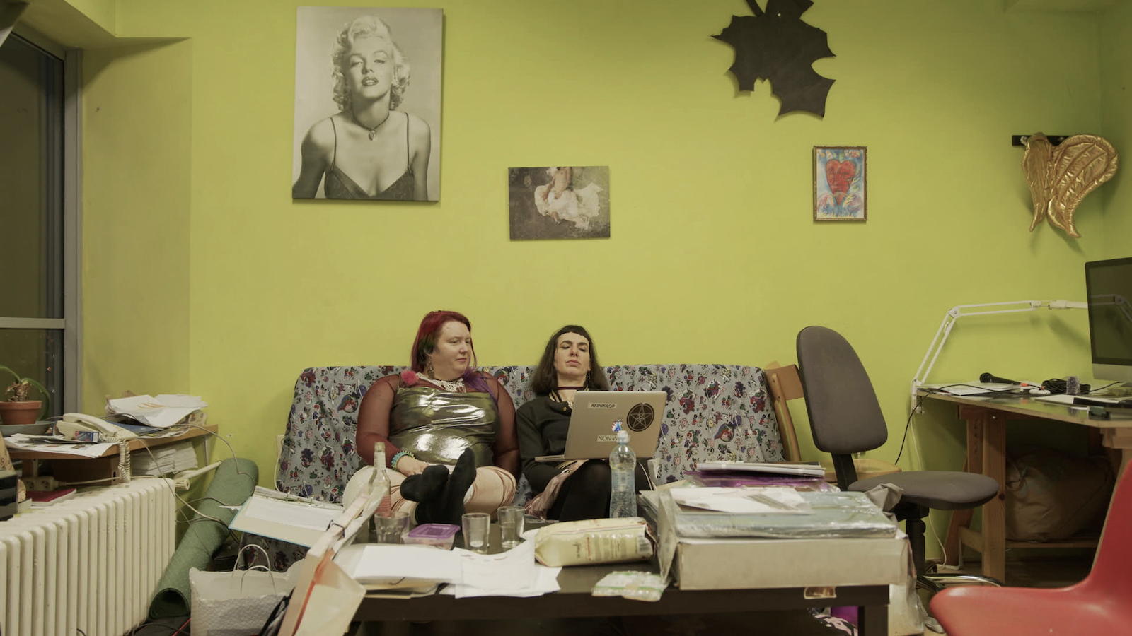 Two women sit on a flowered couch against a lime green wall