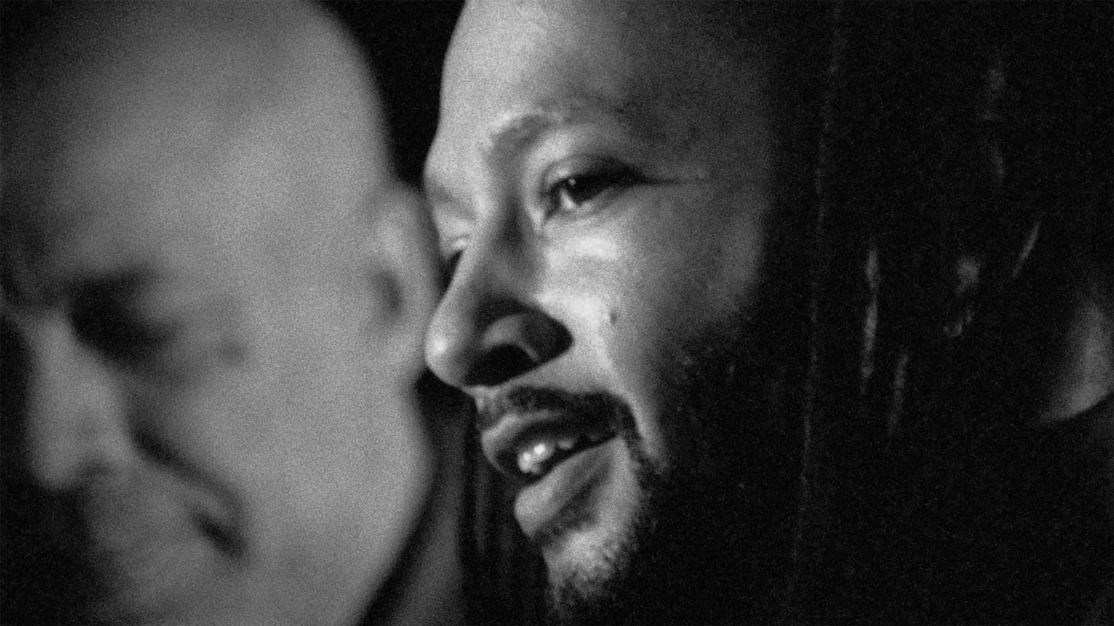 A black and white closeup of a man in profile with another man in the background