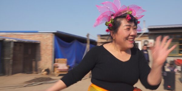 A woman with a flowery pink hat dances outside