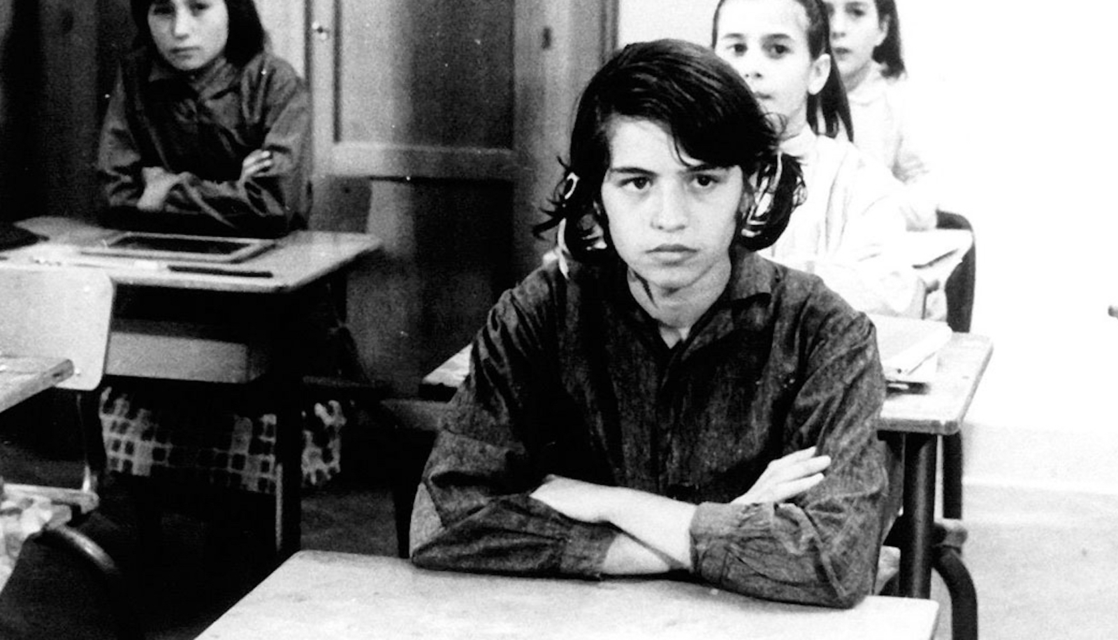 A young girl sits with her arms crossed in a school classroom