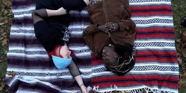 Two young women lie on a blanket outside talking to each other, the image is upside down
