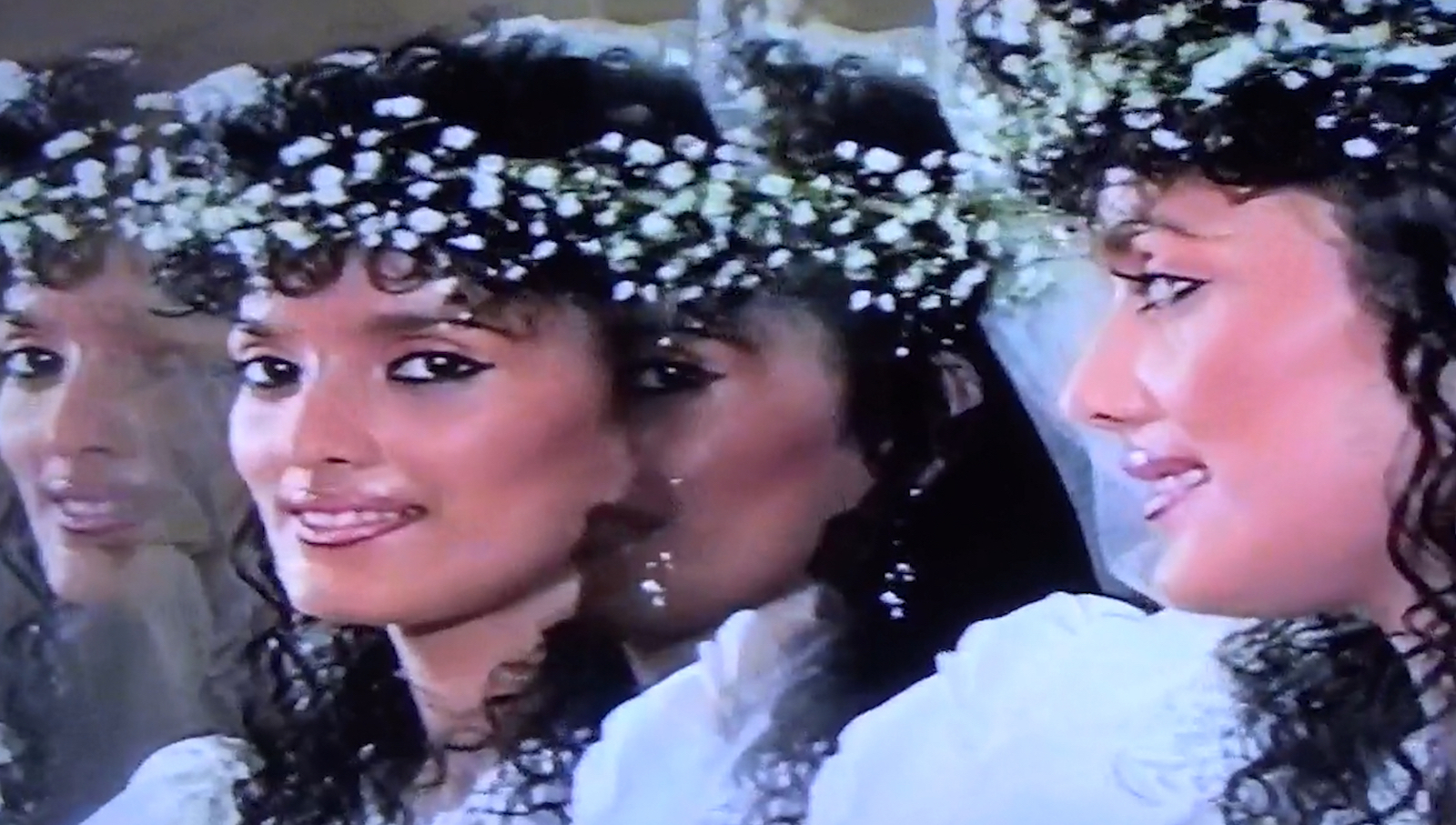 A low-grade video image of a woman in a wedding dress and flowers in her hair, her profile reflected prismatically across the screen