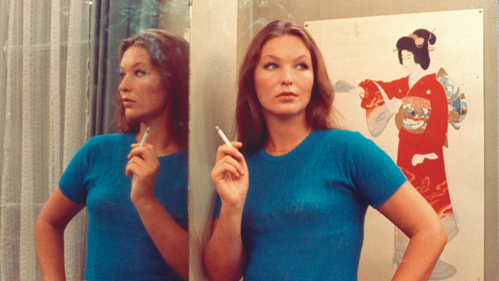 Two or Three Things I Know About Her A woman in a blue shirt smoking a cigarette stands in front of a painting of a geisha in red and next to a mirror