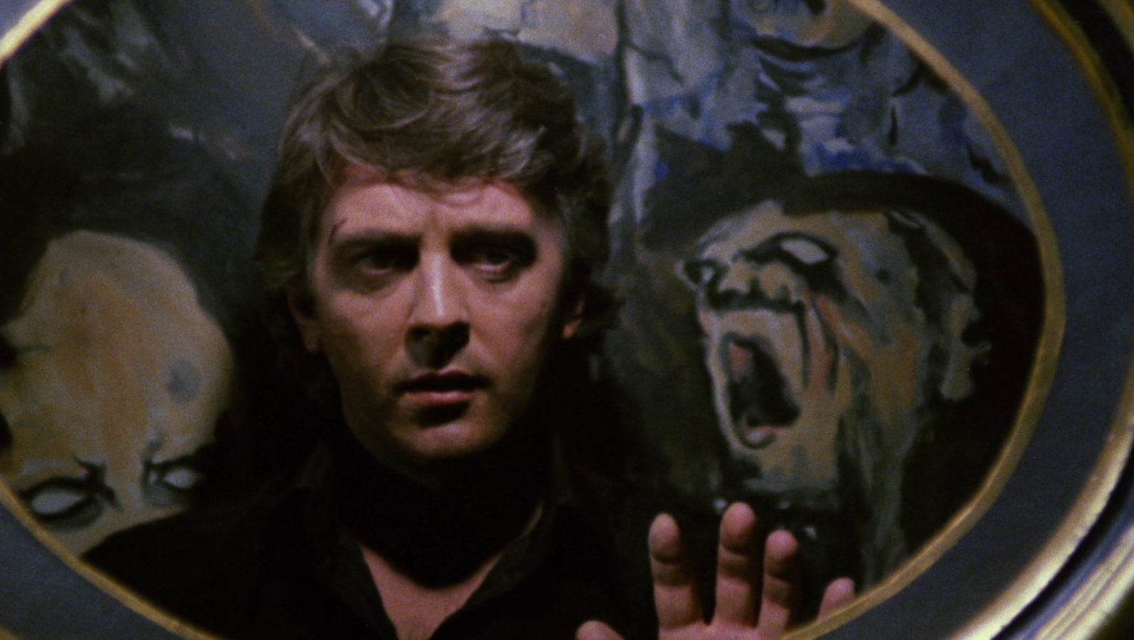 A man touches a mirror, surrounded by a painting of goblin faces