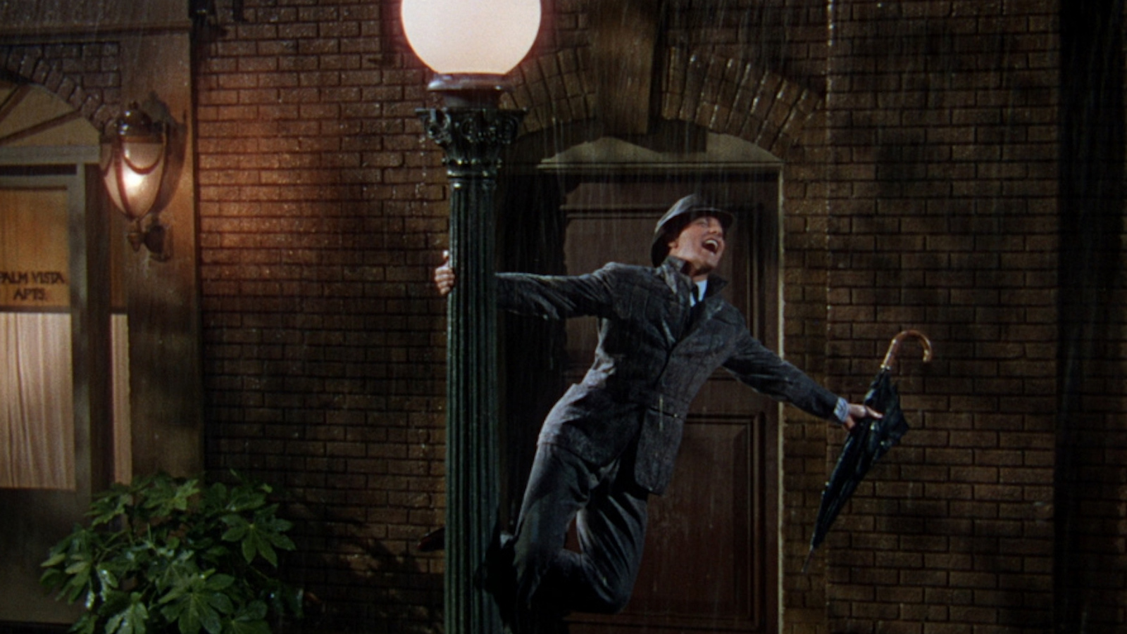 A man sings in the rain while clutching a streetlamp