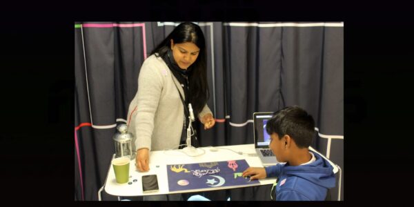 A teacher stands in front of a work table, instructing a child with construction paper and cut outs