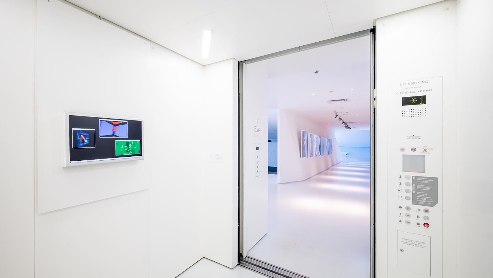 MOMI_REFRESHING THE LOOP_ELEV-14_WEB A white elevator from the inside, with the door open, and a screen on the side