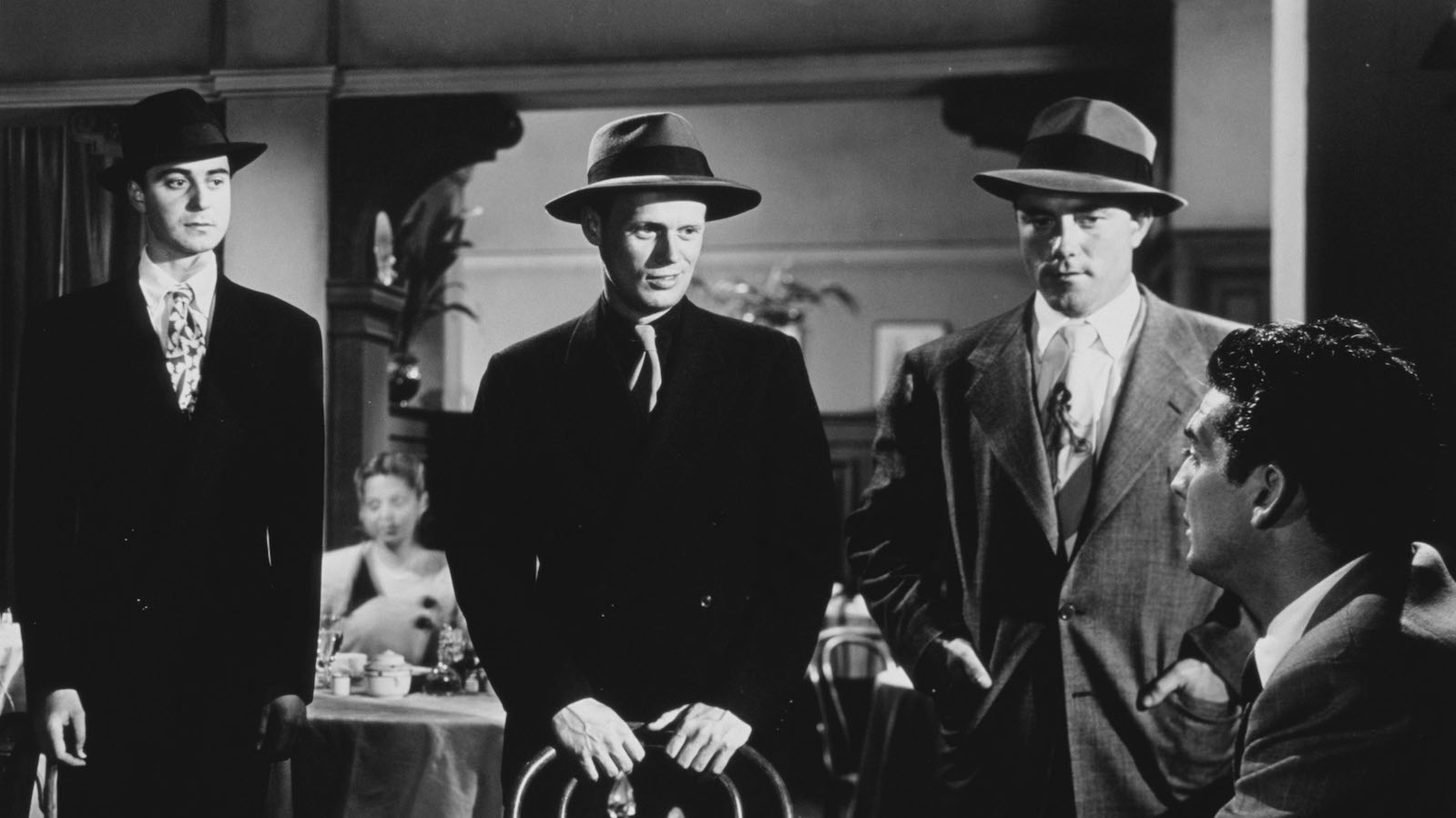 kiss of death 1947 Three menacing gangsters in fedoras hover over a man sitting at a restaurant table in a black and white image