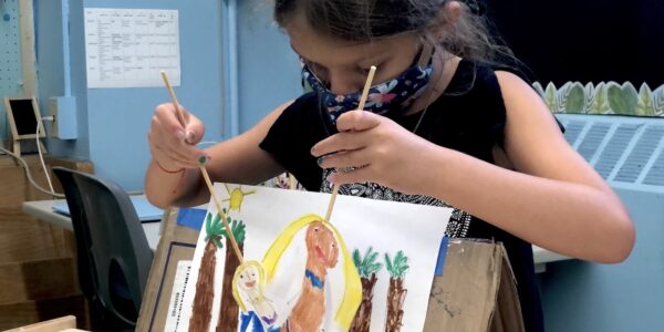 A masked child constructs paper puppets with wooden rods.
