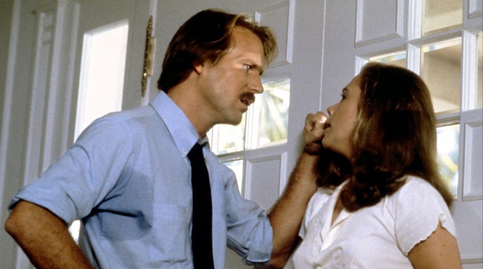 A mustachioed man confronts a blonde woman near a door