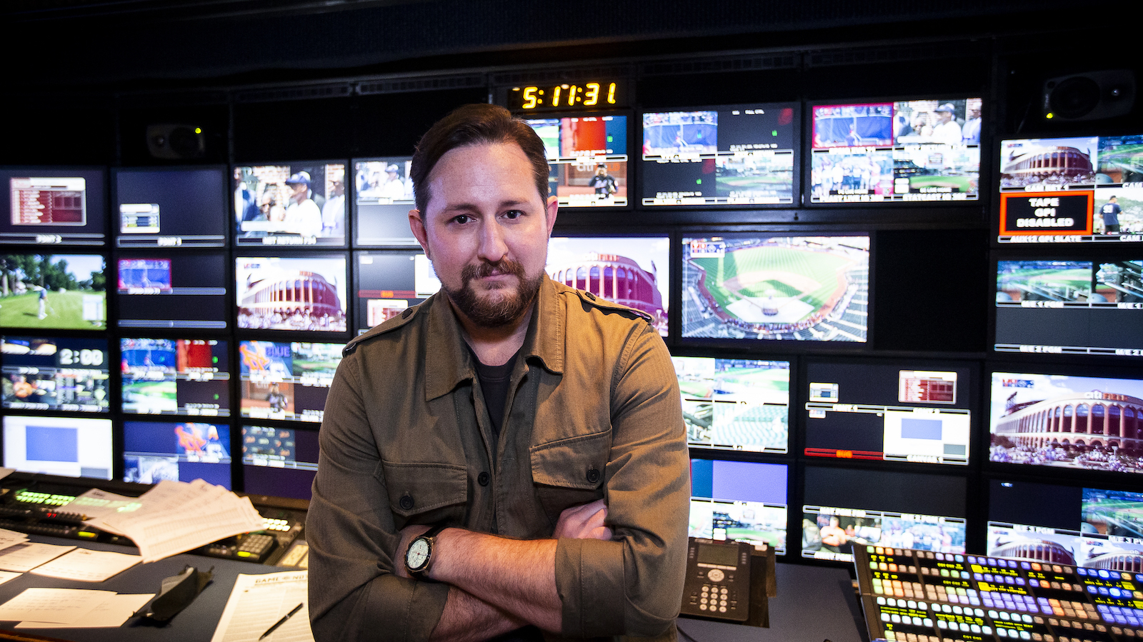 Mets v Phillies A man with a goatee stands with arms folded before a live baseball TV control room, looking at camera