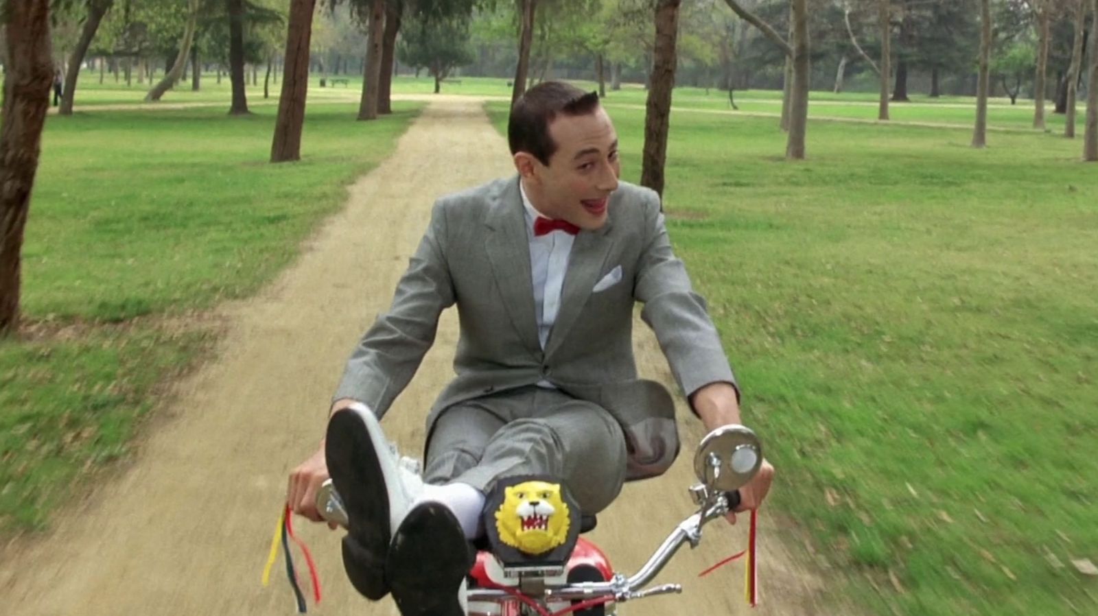 A smiling man rides a bicycle with his legs on the handlebars