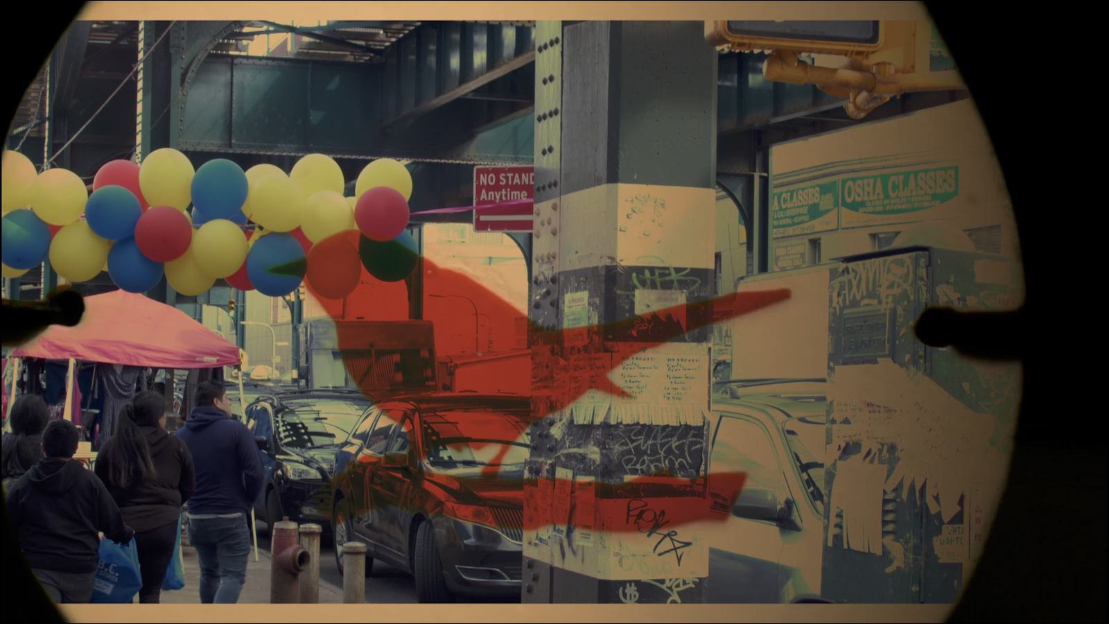 A photo of a New York City street and someone carrying balloons seen through a lens with a red imprint of a bird on it