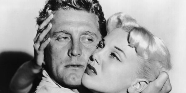 A man and woman hold each other's heads uncomfortably tightly as they look off into the distance in a black and white image