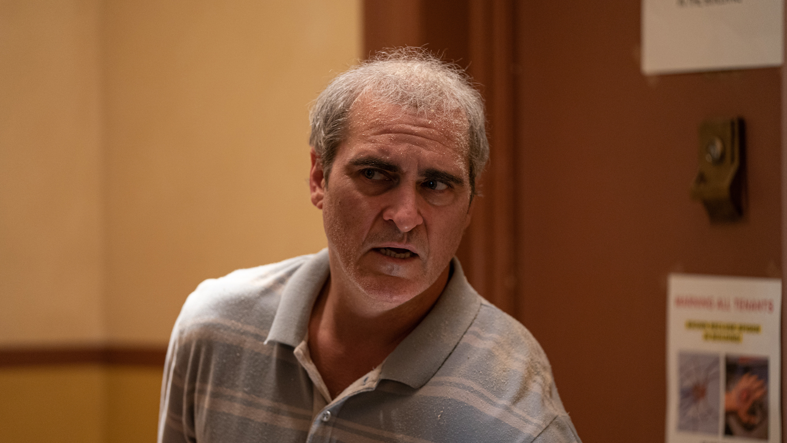 A gray-haired man looks afraid as he peers down a hall