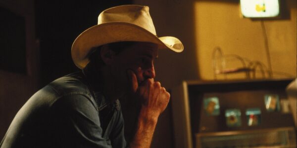 A man in shadow in a motel room wearing a stetson in profile