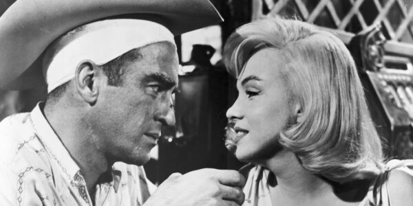 Black and white shot of a man and woman looking at each other in close up. He wears a cowboy hat