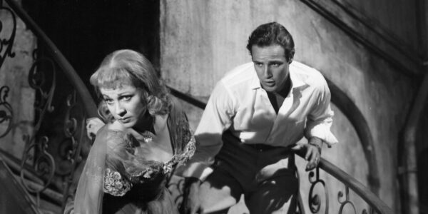 A man on a staircase grabs a woman by the arm as she tries to descend in front of him