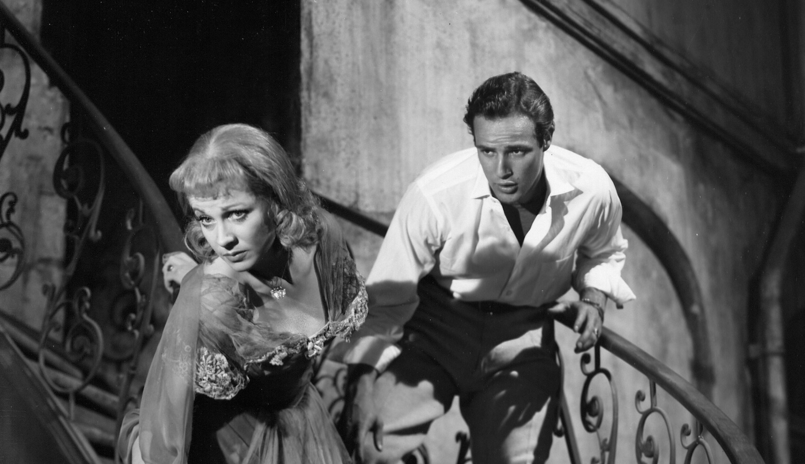A man on a staircase grabs a woman by the arm as she tries to descend in front of him