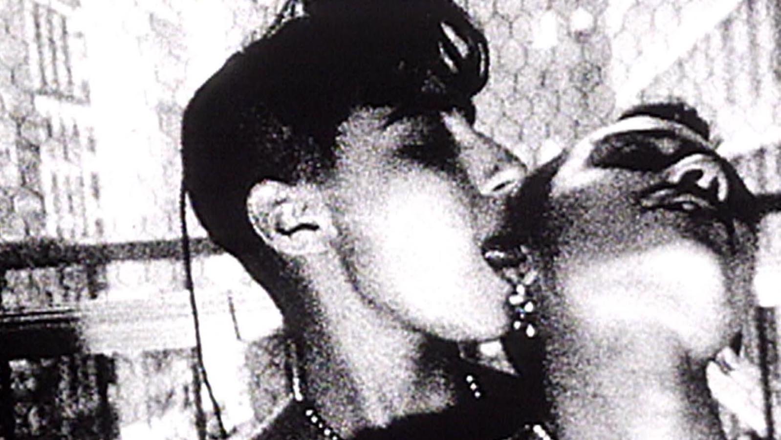 A woman sticks her tongue in another woman's ear in a grainy black and white image