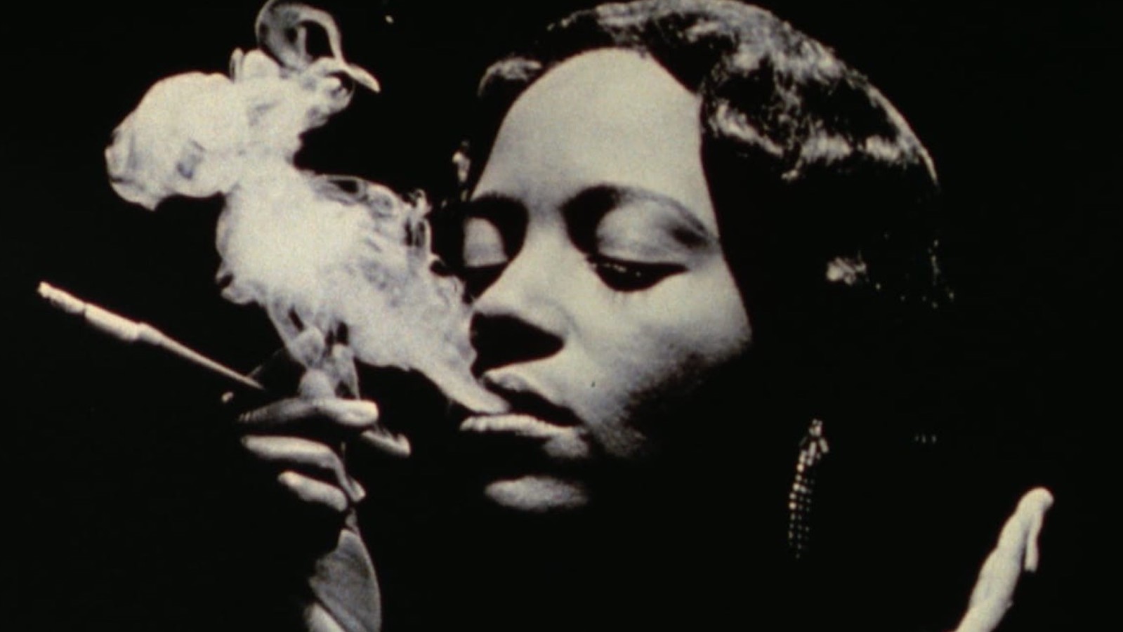 black and white image of a woman smoking, holding a cigarette holder, with her eyes closed and smoke out of her mouth like vapor