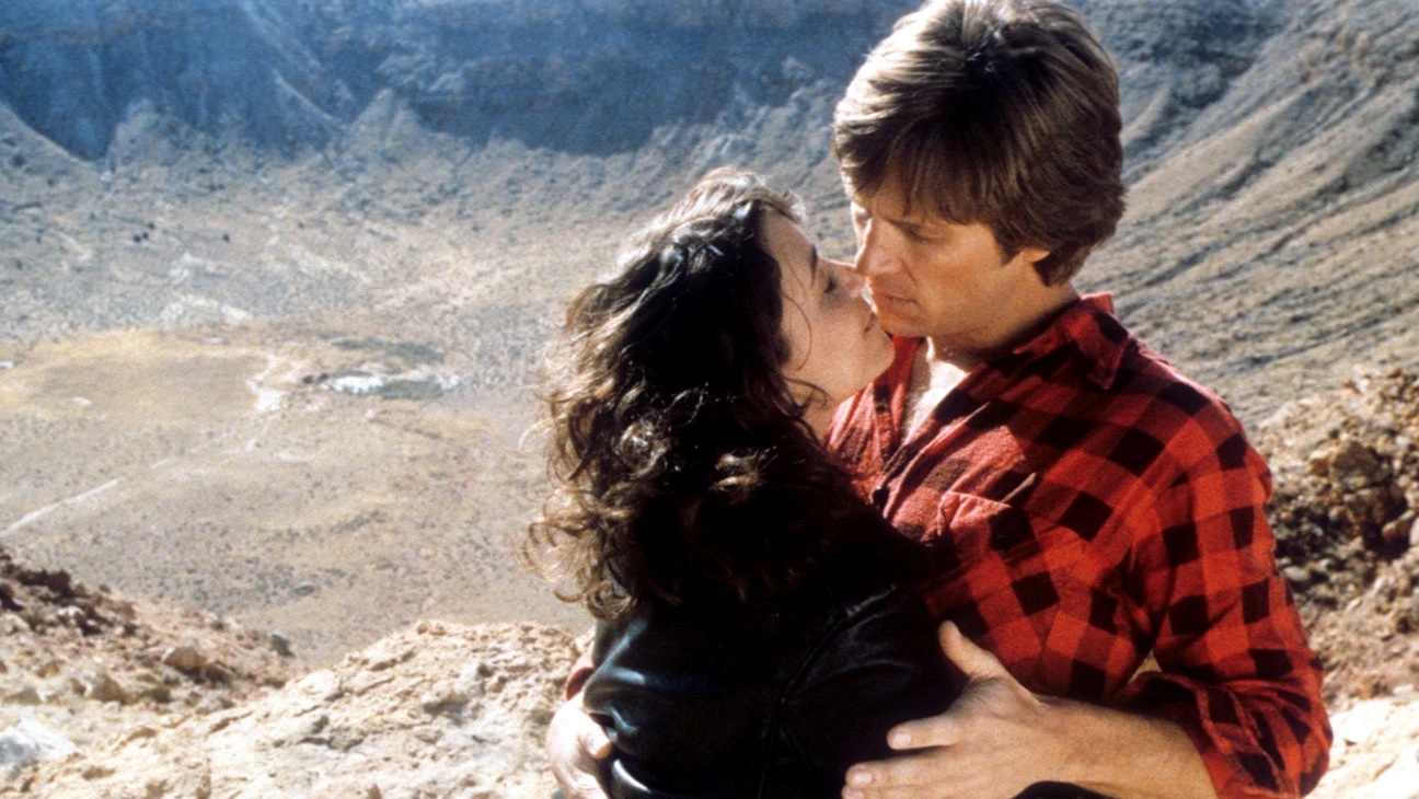 A man and woman embrace against a mountainous backdrop