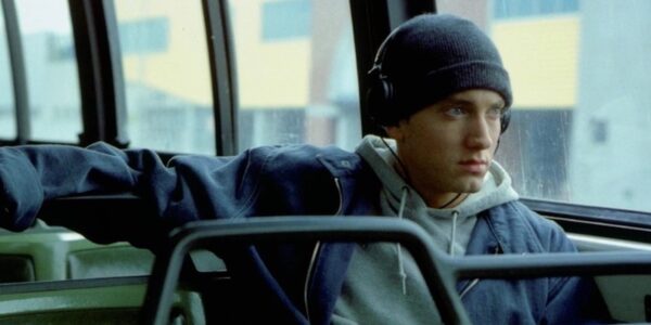 A man in a skull cap sits on a bus with headphones on looking out the window