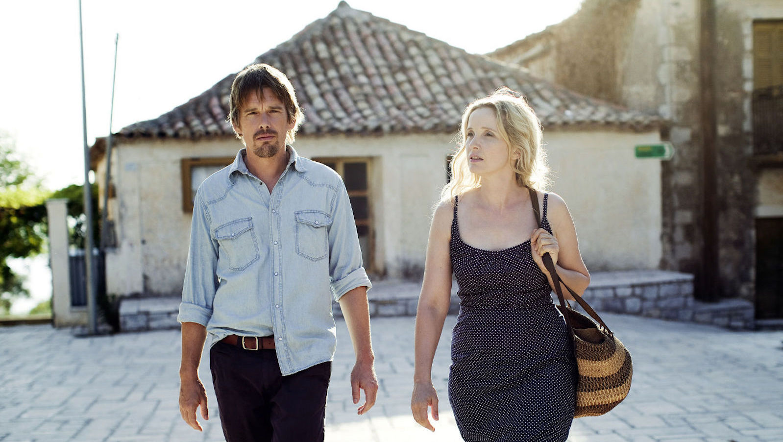 A man and woman walking outside on a cobblestone street towards camera in summer clothes