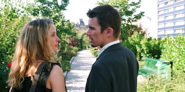 A man and woman look at each other intently in profile in a sunny park