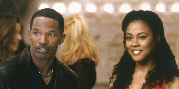 A man and a woman standing together look off screen and smile