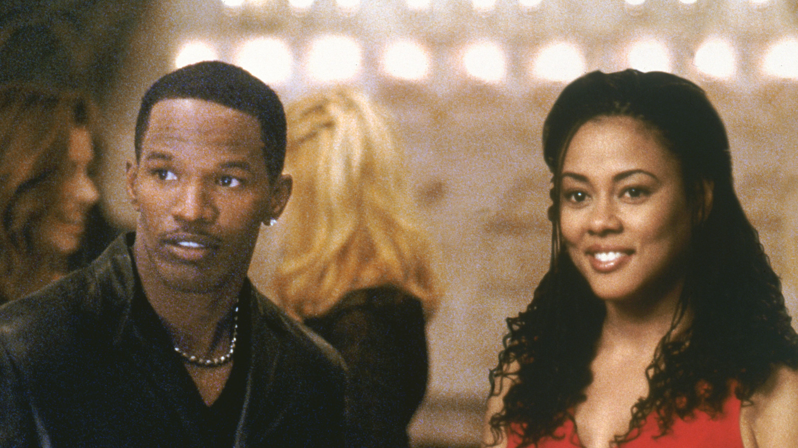 A man and a woman standing together look off screen and smile