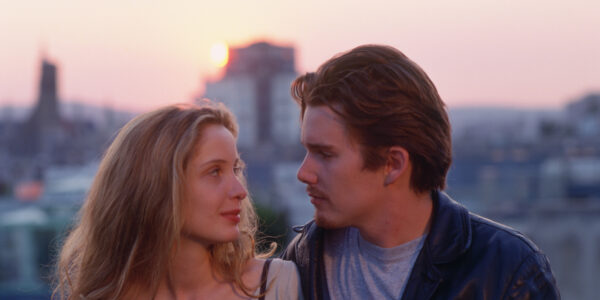 A young man and woman looking at each other sitting outside in front of a sunset