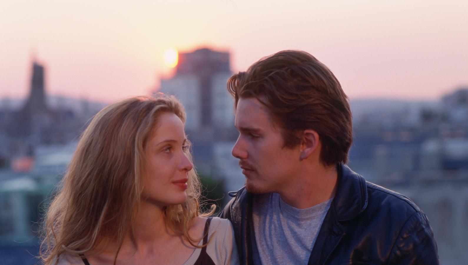 A young man and woman looking at each other sitting outside in front of a sunset