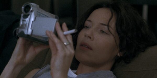 A woman holds a cigarette and looks at a camcorder viewfinder