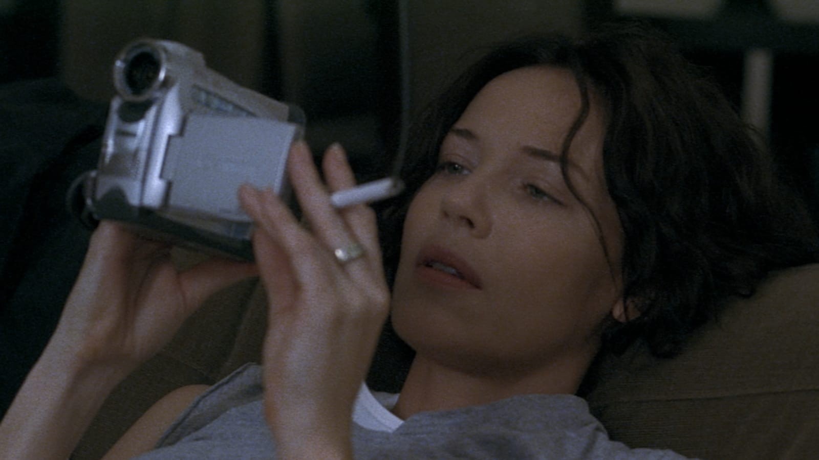 A woman holds a cigarette and looks at a camcorder viewfinder