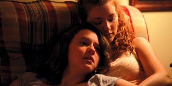 Two young woman sit on a couch, holding each other