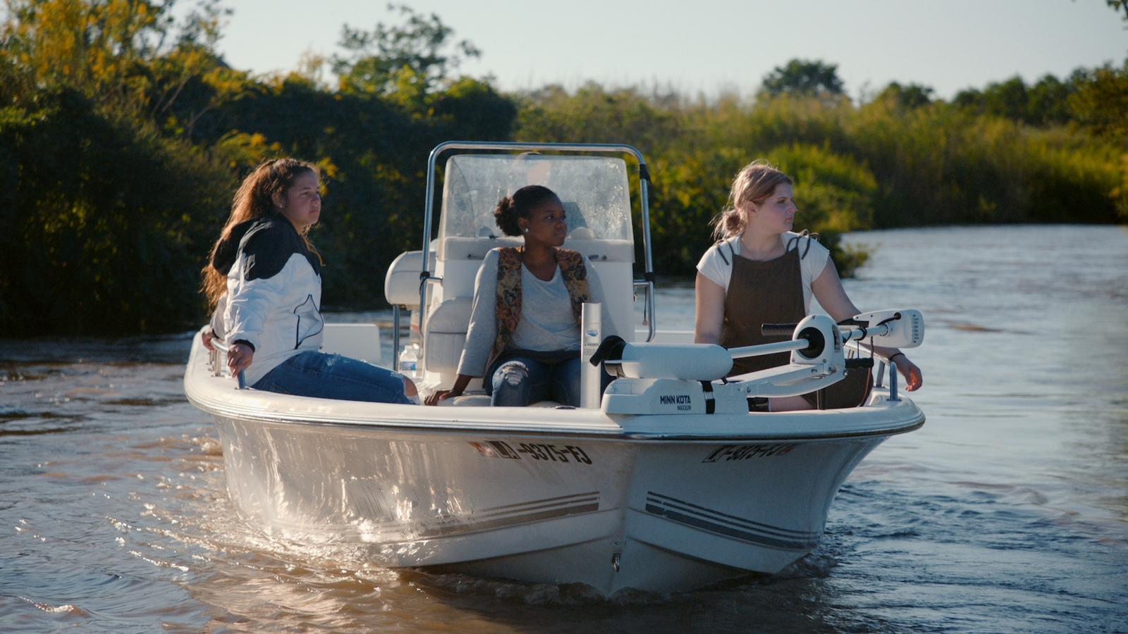 Three women sit in a motorboat moving up a river in the sunlight