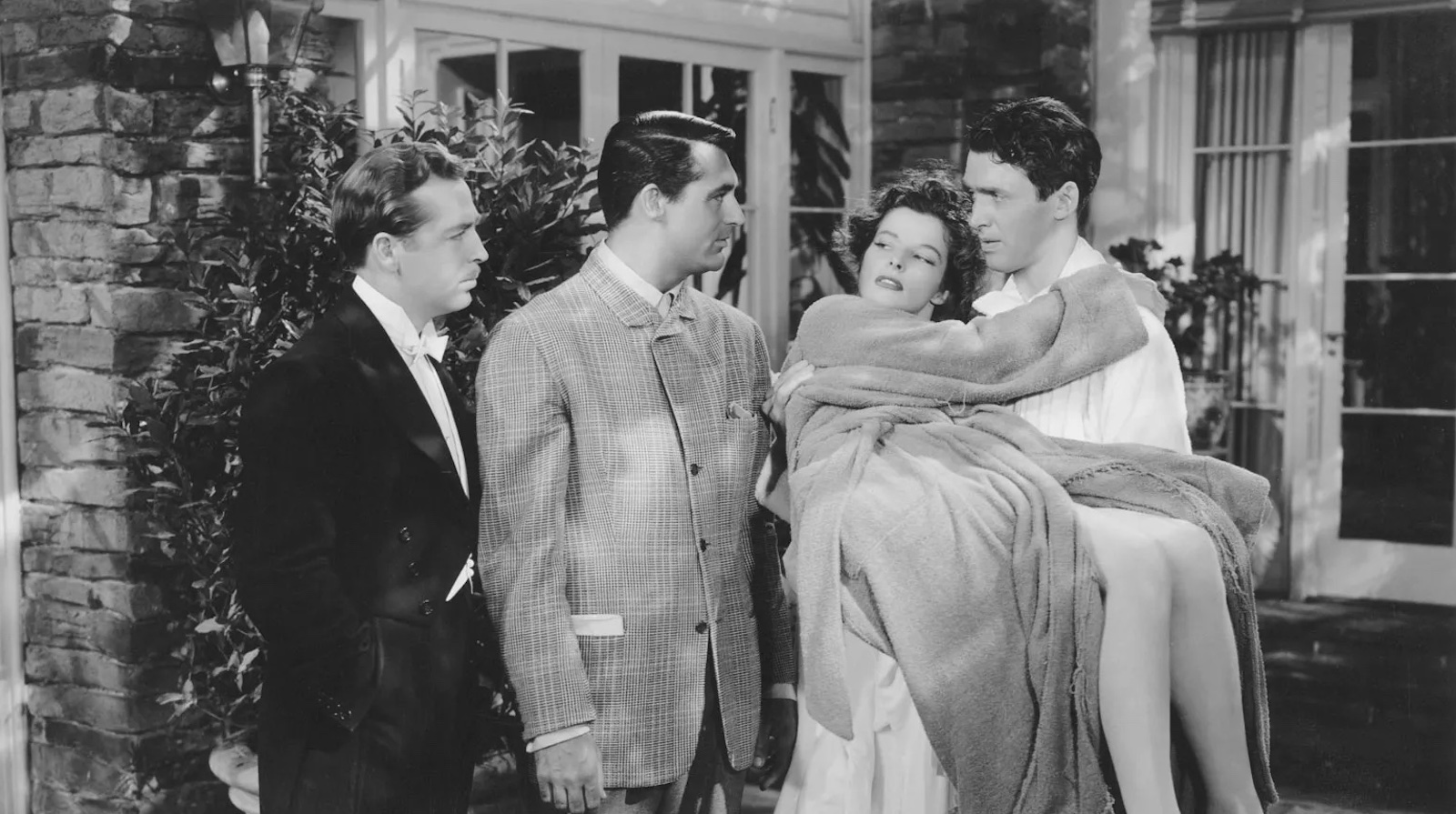 A woman is carried by a man, with two other men standing to her right