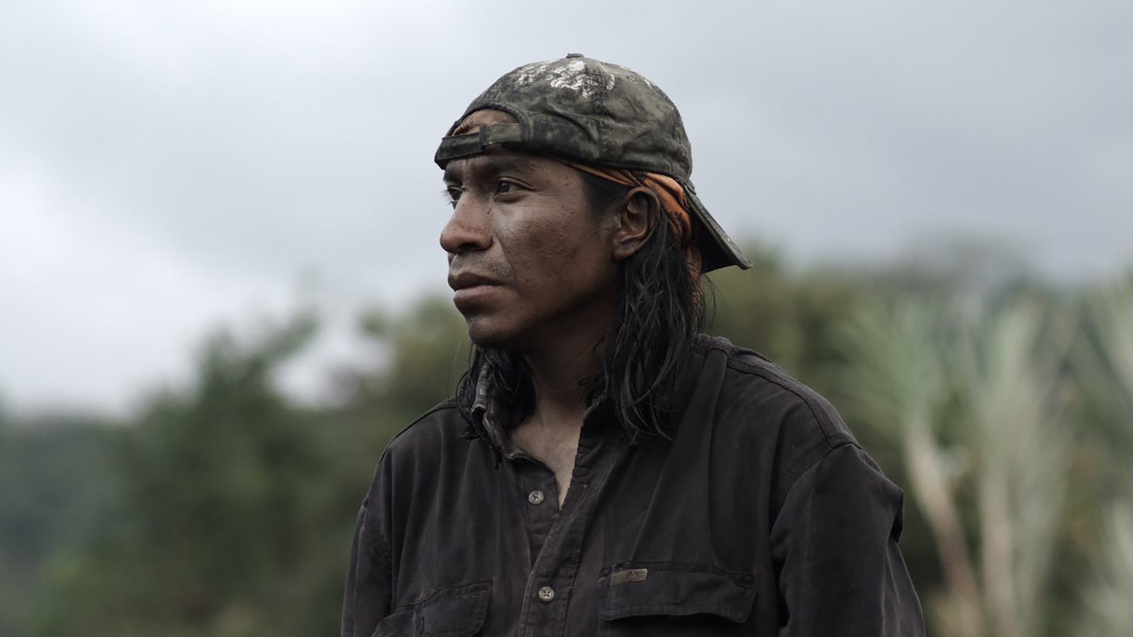 Roza1 A man in a dirty backwards baseball cap and long hair looks off into the distance