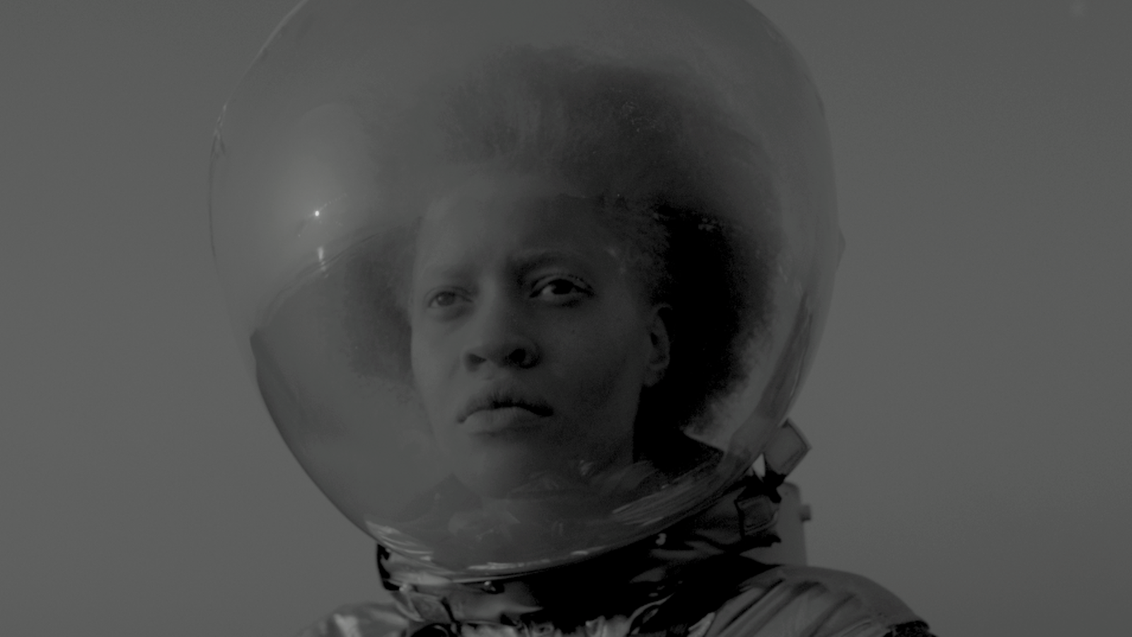 black and white image of a young black woman wearing a globe-like space helmet on her head