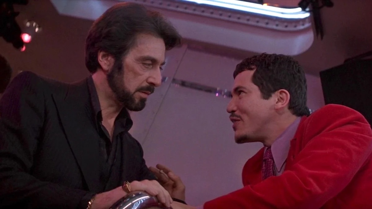 carlitos-way From a low angle image, a man with a beard looks intently at a shorter man in a red jacket