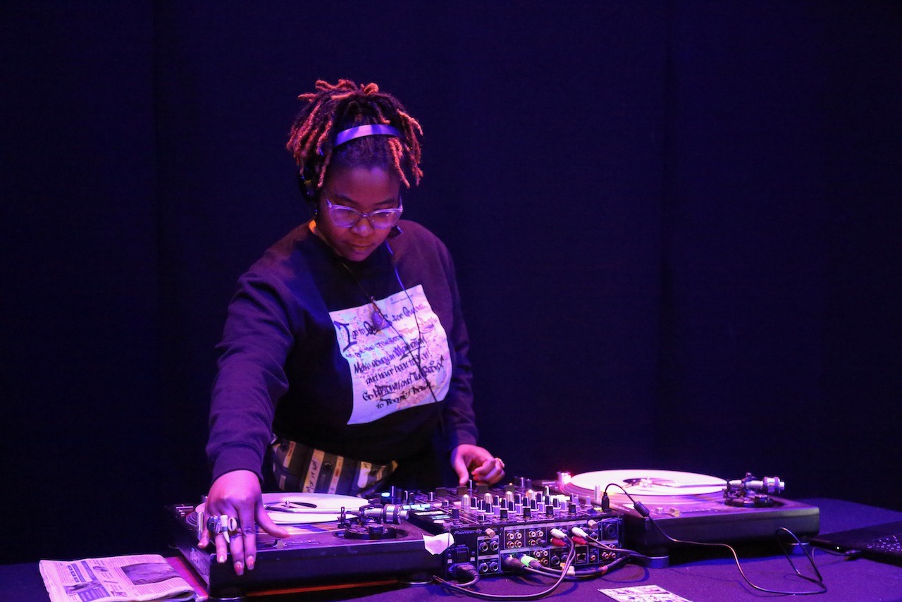 A black woman spins records at a DJ station