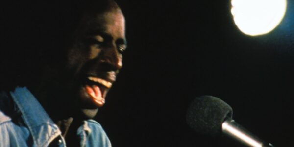 A man screams into a microphone against a black background