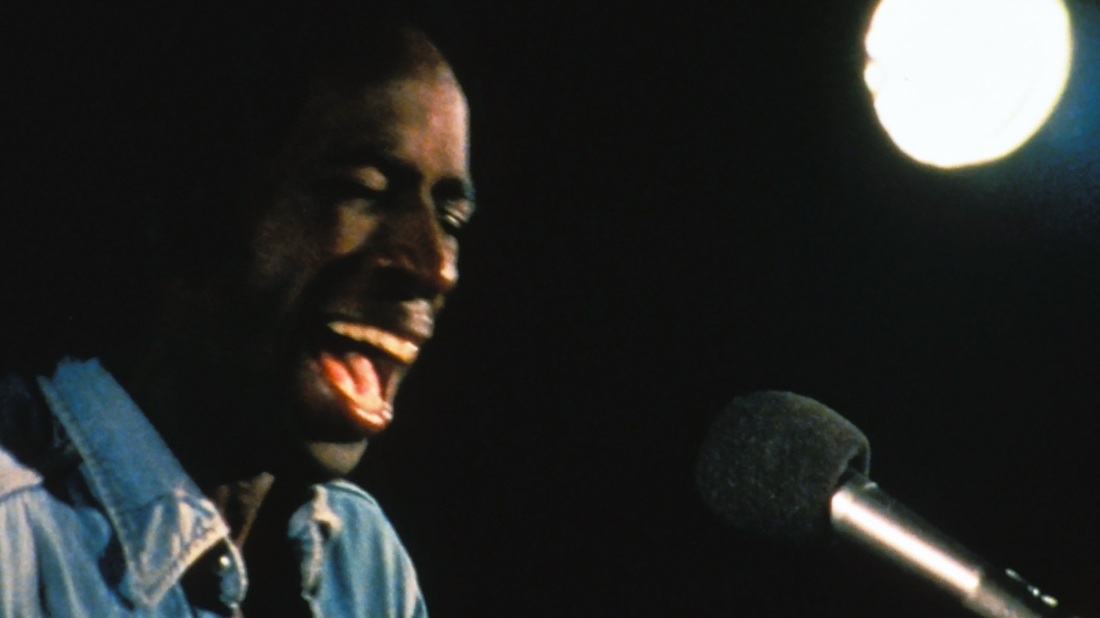 A man screams into a microphone against a black background